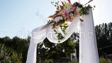 在阳光明媚的夏日，婚礼拱门装饰着鲜花。 节日花装饰。 玫瑰和羽毛草